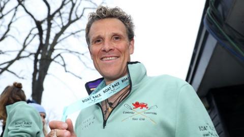 James Cracknell smiling while wearing a Cambridge University boat club top and holding a rowing medal
