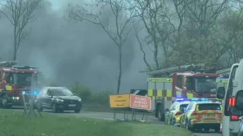 BBC A road side image of black smoke in the air, and emergency service vehicles in Sutton. 