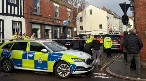 BBC A police car with people in front of a cordon