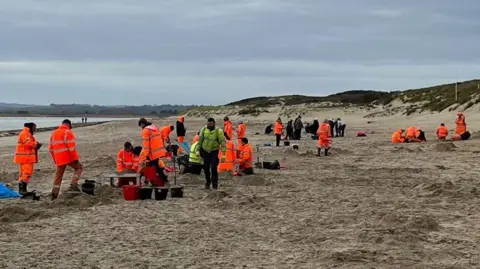 People in hi-viz jackets engaged in a clean up operation on Camber Sands