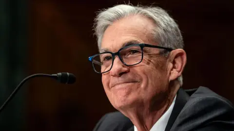 Getty Images A smiling Jerome Powell, dressed in a dark grey suit, sits in front of a microphone