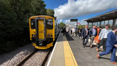 A yellow GWR train at a platform. There are people walking towards the camera on the right.