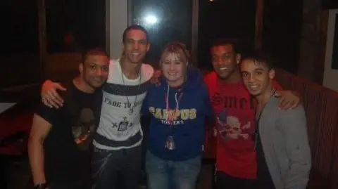 Supplied Debbie Travis-Walker, in a blue hoodie, is smiling at the camera alongside four members of the band JLS. They have short hair cuts and are smiling.