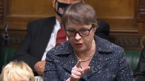 PA Media Woman gesturing while making a point in Parliament. Maria Eagle is sitting on the back benches, wearing glasses, with brown hair, and a navy patterned blazer