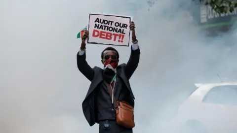 AFP A demonstrator holds a placard as a cloud of tear gas surrounds him during anti-government protests in Nairobi on July 16, 2024.