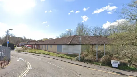 Google A Google street view image of the Living Ambitions property on Canal Street, Kirkintilloch. The single story brick building is to the right of the street. It has metal panels covering the windows. 