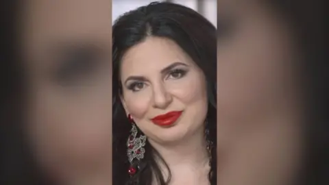 Dr Ruja Ignatova has long black hair and wears bright red lipstick and silver and red earrings