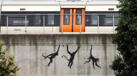 Banksy Three monkeys hanging from bridge 