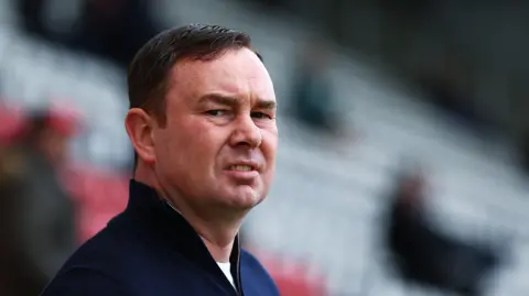 Morecambe boss Derek Adams looks on