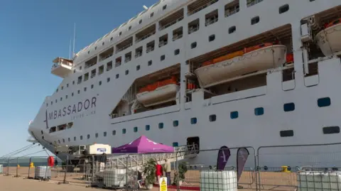 Getty Images A large cruise ship berthed at Invergordon. The boat is white and several storeys high. The word "Ambassador" is in purple on the side of the ship.