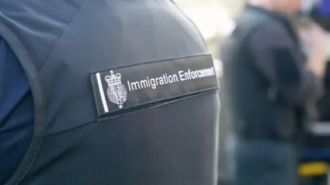 A zoomed in photo a person wearing an Immigration Enforcement uniform which is navy blue in colour. 