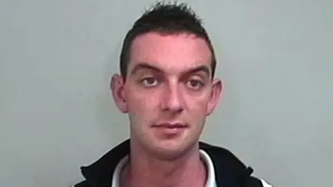 PA Media A man with short dark hair looking towards the camera wearing a black vest over a white shirt