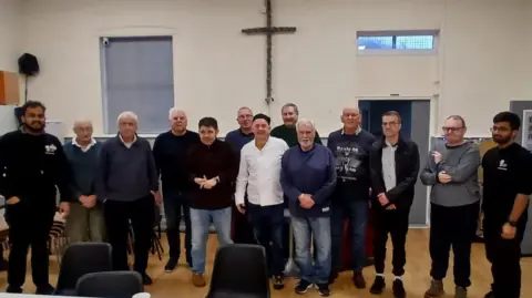 Contributed A group of men stand beside one another smiling at the camera. Chairs are pictured in front of them.