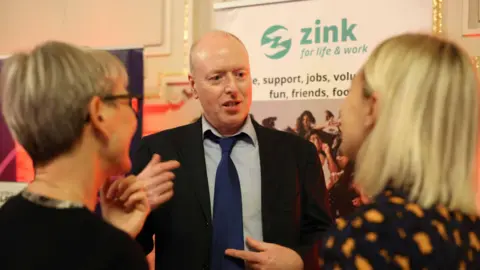 Zink A man wearing a black suit, blue shirt and blue tie at an awards evening
