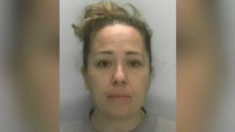 South West ROCU Custody photograph of a person with their hair tied up, wearing a light-coloured top, against a plain background.