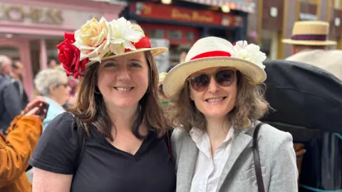 Two women wearing straw hats donned with red and white roses 