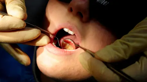 PA Media Dentist uses tools to examine a child's teeth