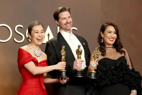 Getty Images KPop Demon Hunters film-makers Maggie Kang, Chris Appelhans and Michelle LM Wong pose with their Oscars statuettes.