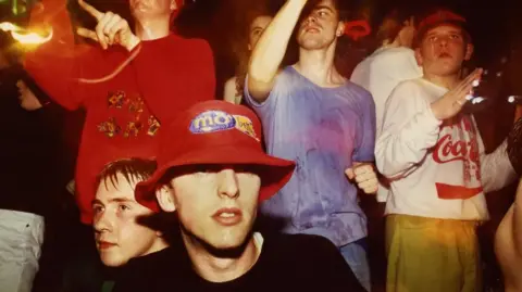 Tony Davis / British Culture Archive  A group of ravers dancing at The Eclipse club in Coventry. They are wearing an array of bright clothes and a range of hats 