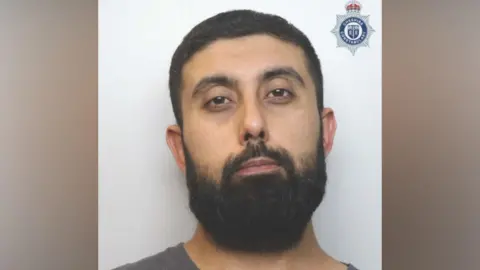 Cheshire Police Asad Hussain, a man with short dark hair and a large black beard, poses in a police mugshot.