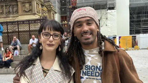 A woman and a man stand smiling in a square.