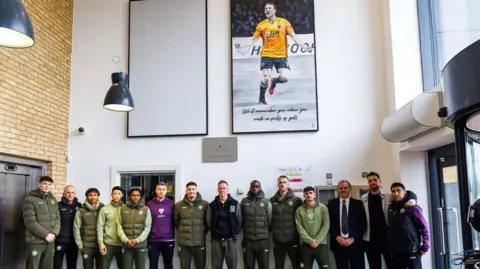A football team posing underneath two large paintings hanging in the entrance of a building