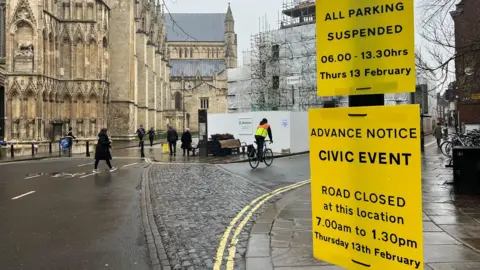 Two yellow notices near York Minster, warning of a civic event and road closure between 07:00 and 13:30 GMT on 13 February.