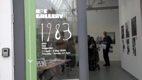 Alan Van Wijgerden The glass door of Art Riot Collective has an advert for 1983 in white lettering. 