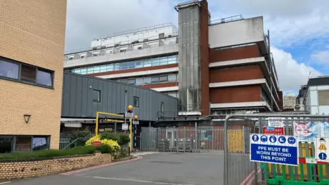 Sam Read/BBC Wood and brick hospital buildings with a fenced-off construction site in the foreground