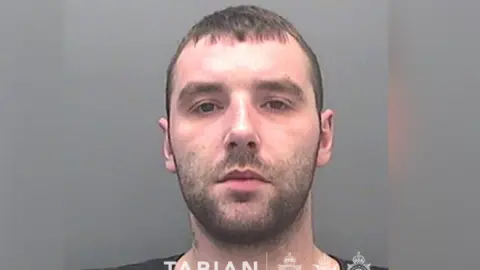 A custody image of David Braddon. He has dark stubble and looks at the camera with a neutral expression. 