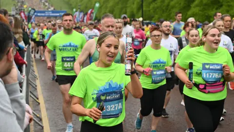 Pacemaker A women in a green Belfast marathon shirt holds a relay baton and holds it up to the camera.