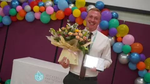 Wickersley Partnership Trust Josh Bartle, a modern languages teacher and senior leader at Clifton Community School in Rotherham, holding his silver award for teaching with a bouquet of flowers and balloons behind.