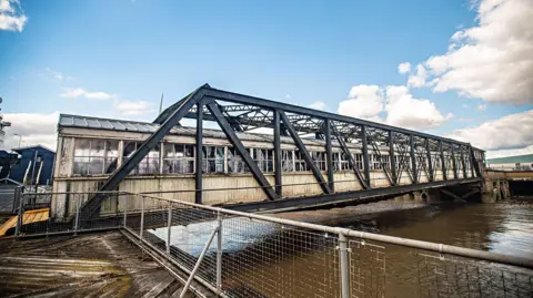 Evewright Arts Foundation A bridge on Tilbury Port. It looks like a greenhouse and has artwork to honour the Windrush generation