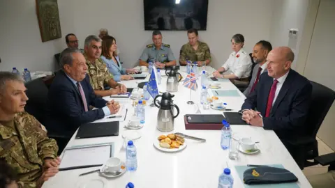 PA Vasilis Palmas and John Healey sit at a white table with various military generals