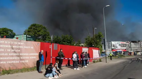 Getty Images People waiting outside the Marywilska shopping centre as a massive cloud of black smoke comes out of it.