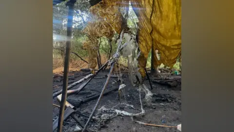 Little Wild Tribe The aftermath of the fire shows a blackened ground with burned wood, and a yellow piece of canopy drape with burn holes in it.