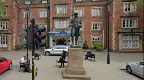 The bronze statue of potter Josiah Wedgwood outside the North Stafford Hotel in Stoke-on-Trent. A couple of people sit on nearby benches.