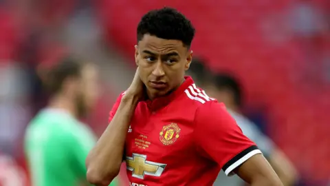 PA Media Image of footballer Jesse Lingard during a match for Manchester United taken in Many 2018. He is wearing a red Manchester United kit and has one hand on his hip and the other resting on his neck and back of his head. 