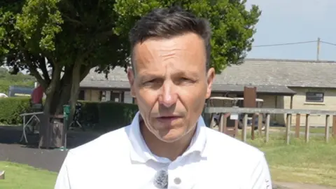 Jamie Niblock/BBC Mark Payne looks at the camera. He has short dark hair and wears a white polo top.
