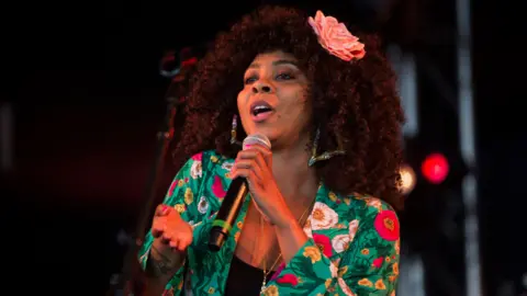 Hollie Cook singing on stage in a colourful floral jacket.