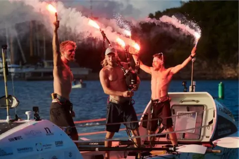 MacLean brothers The three brothers celebrate completing their Atlantic challenge holding flares and playing the bagpipes.