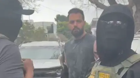 Reza, who appears to be a young man in his early 30s, is handcuffed by masked immigration officials