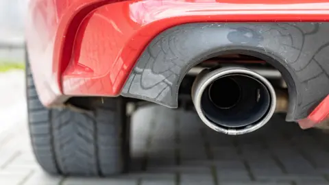 Getty Images Stock photo shows a close up of a red car's exhaust pipe while parked on a driveway.