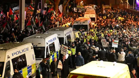 Getty Images Police vans and officers are seen among a large group of people, some holding banners and flags