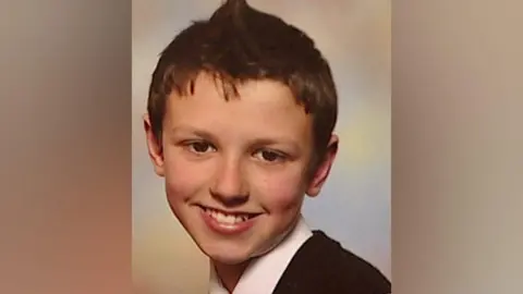 Oliver King has short brown hair and is wearing a white shirt and a dark-coloured top. He is smiling at the camera.
