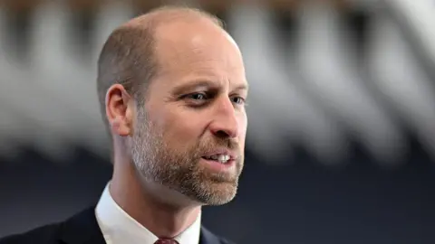 A close-up of Prince William, during a visit to Wales in December 2025. He is wearing a suit with a red tie. 