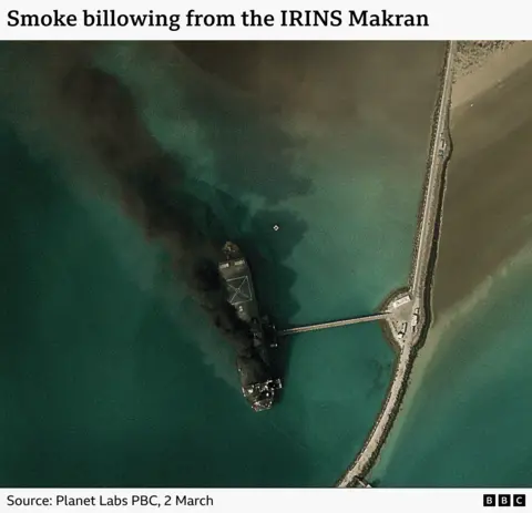 A satellite image showing an Iranian ship ablaze in a port. The caption reads "Smoke billowing from the IRINS Makran.
