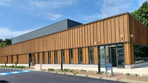 Exterior of the Community Diagnostics Centre in Corby. The structure appears to be covered in a timber-style cladding with glass-panelled front door. 