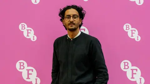 BFI Imran Perretta stands in front of a pink BFI backdrop.
