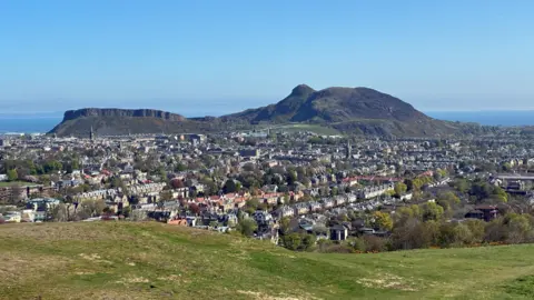 Rod Henderson Edinburgh city and Arthur's Seat in the background. The sky is bright blue and the sea is the background. 